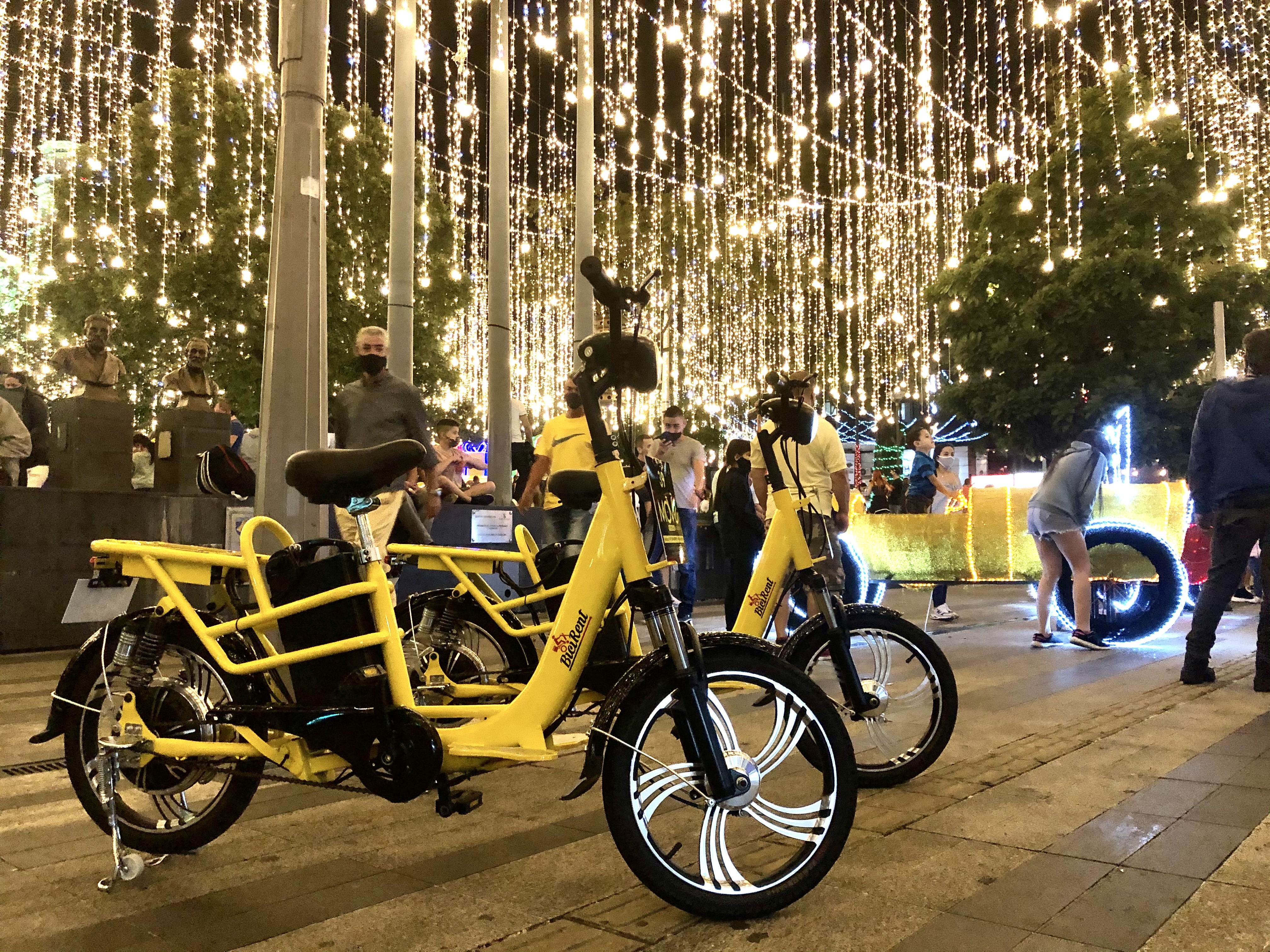Dos bicicletas eléctricas amarillas de MOVE estacionadas bajo una cortina de luces navideñas en Medellín